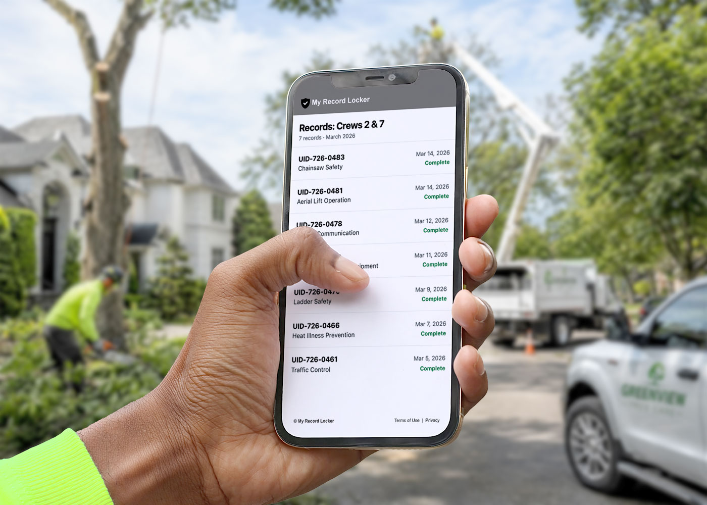 A worker at a job site holding a phone that lists completed training records for their crews.